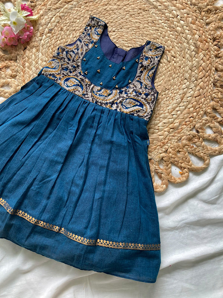 Flat lay view of peacock blue kids traditional dress featuring kalamkari printed yoke embellished with gold beads