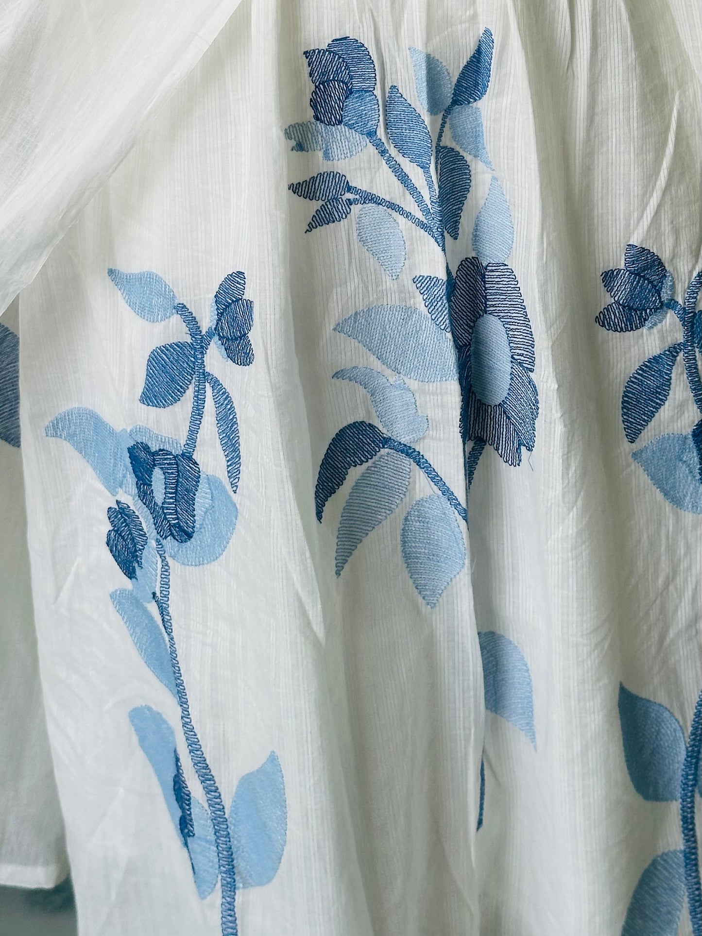 Detailed view of the blue floral machine embroidery on the white mul cotton fabric