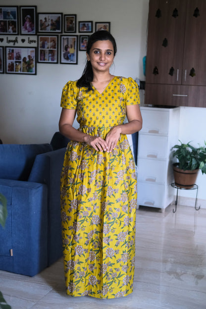 A woman wearing a yellow cotton maxi nighty with a dual floral print and V-neckline.