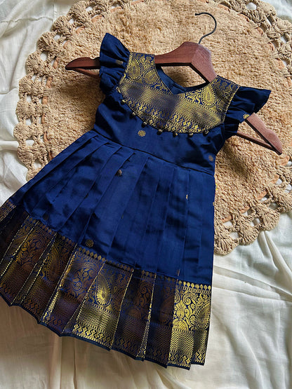Flat lay of royal blue pattu frock for baby girl featuring woven gold paisley yoke and potli trims