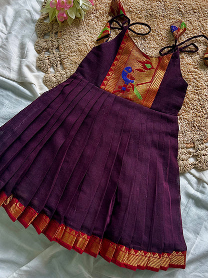 Flat lay of brown kids ethnic frock with shoulder tassels and gold zari hem
