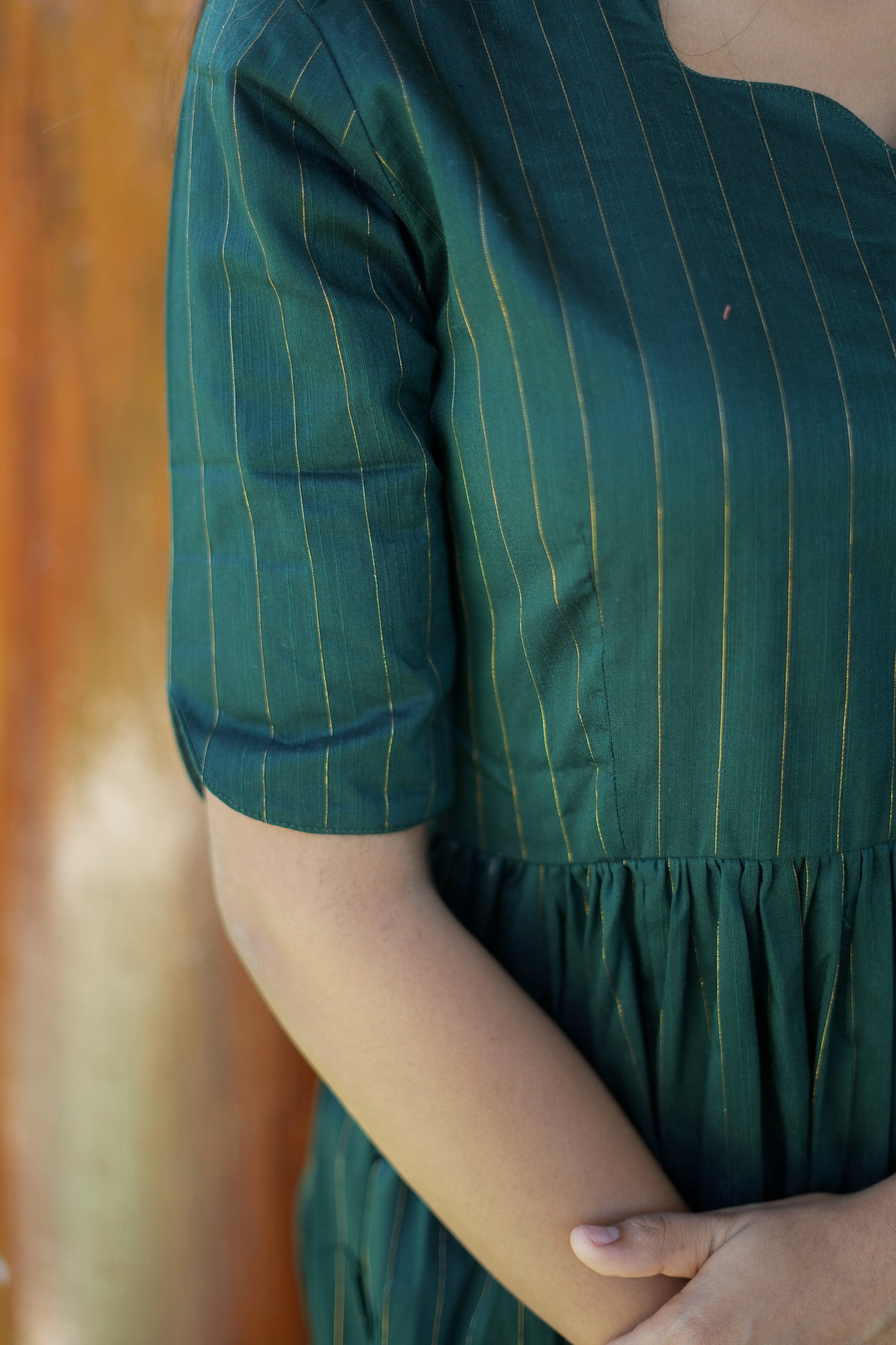 Close-up of the elbow-length sleeve showing the fine gold vertical zari lines woven into the green raw silk fabric.