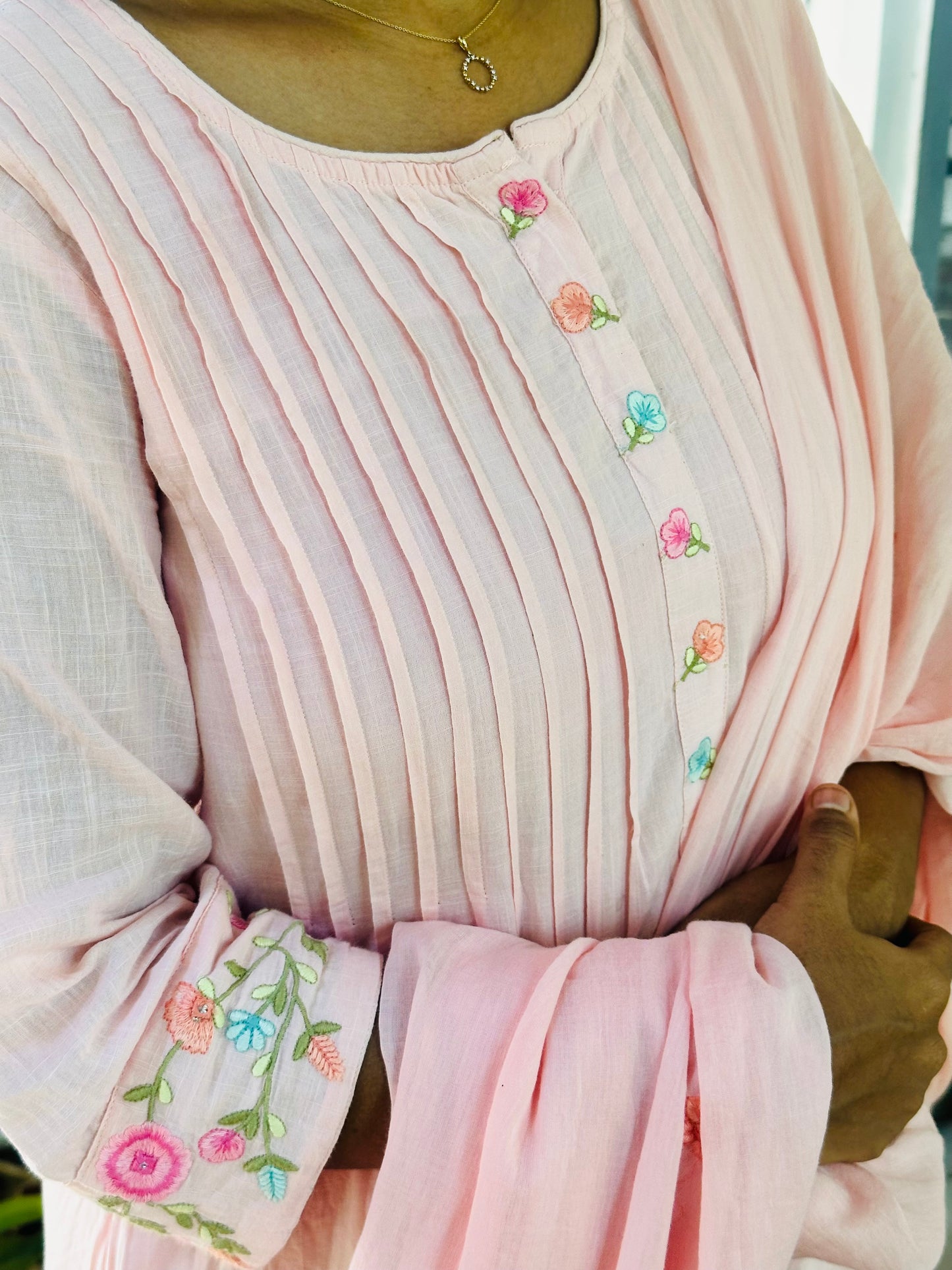 Close-up of the pin tucks and colorful floral embroidery on the neckline and sleeves of the pink cotton kurti.