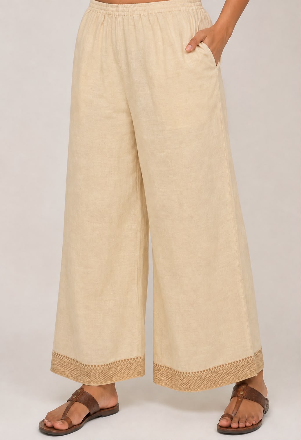 Beige cotton palazzo pants with a traditional embroidered border at the hem and side pockets.