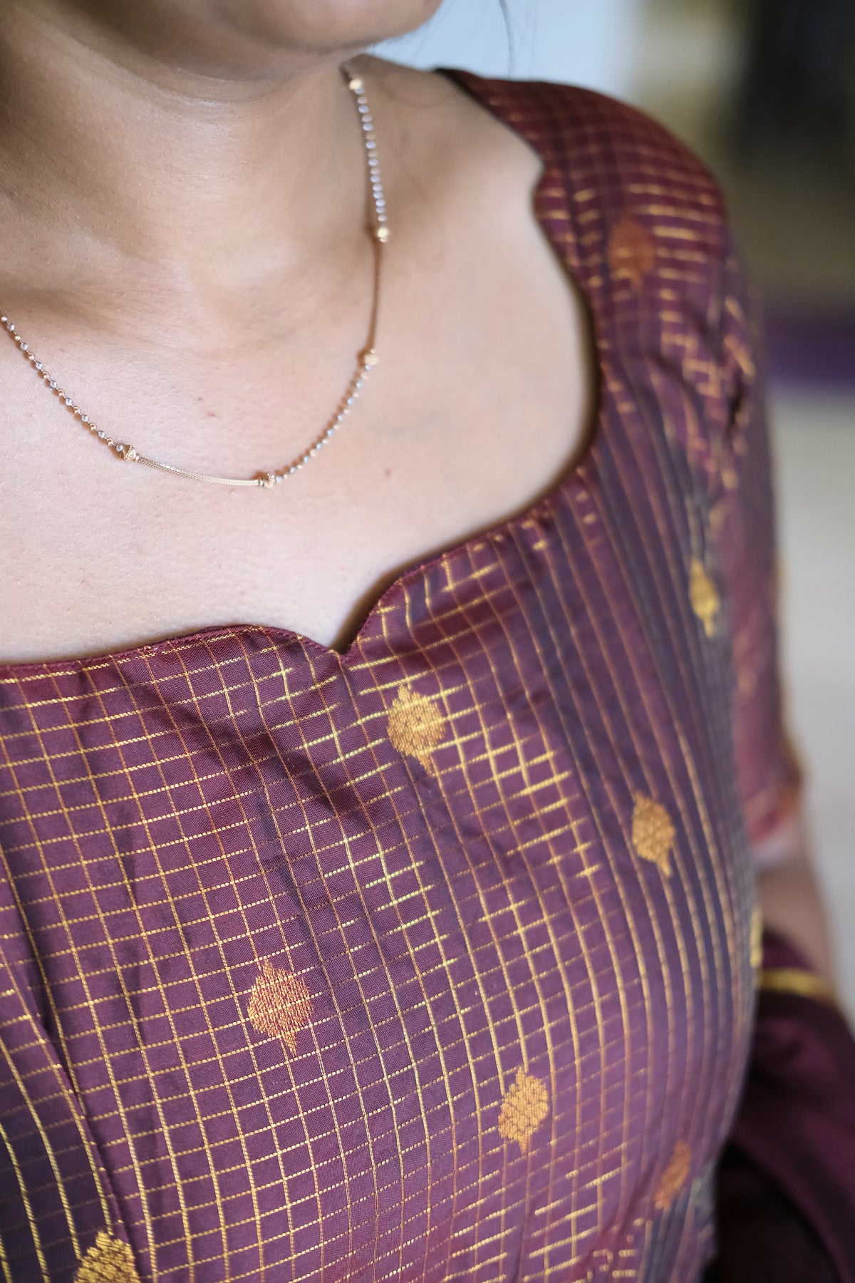 Close up of modified sweetheart dip neckline and golden woven check pattern on maroon silk fabric
