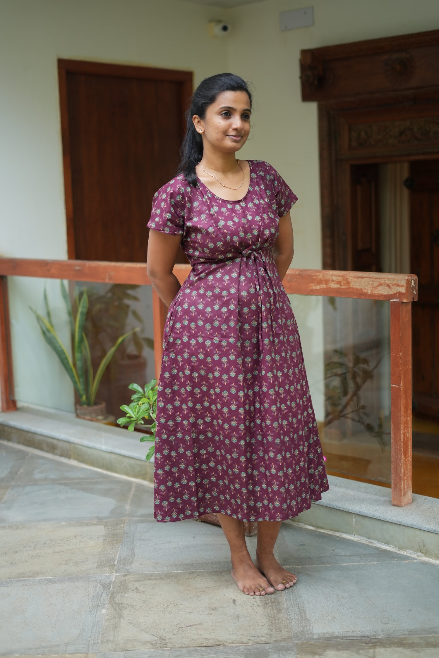 A calf-length dark wine cotton nighty for women featuring green floral prints and an adjustable front waist tie.