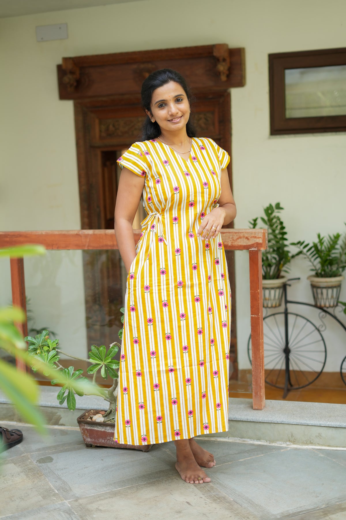 Mustard yellow and white striped cotton nighty for women with pink floral prints, featuring a V-neck and side tie waist.