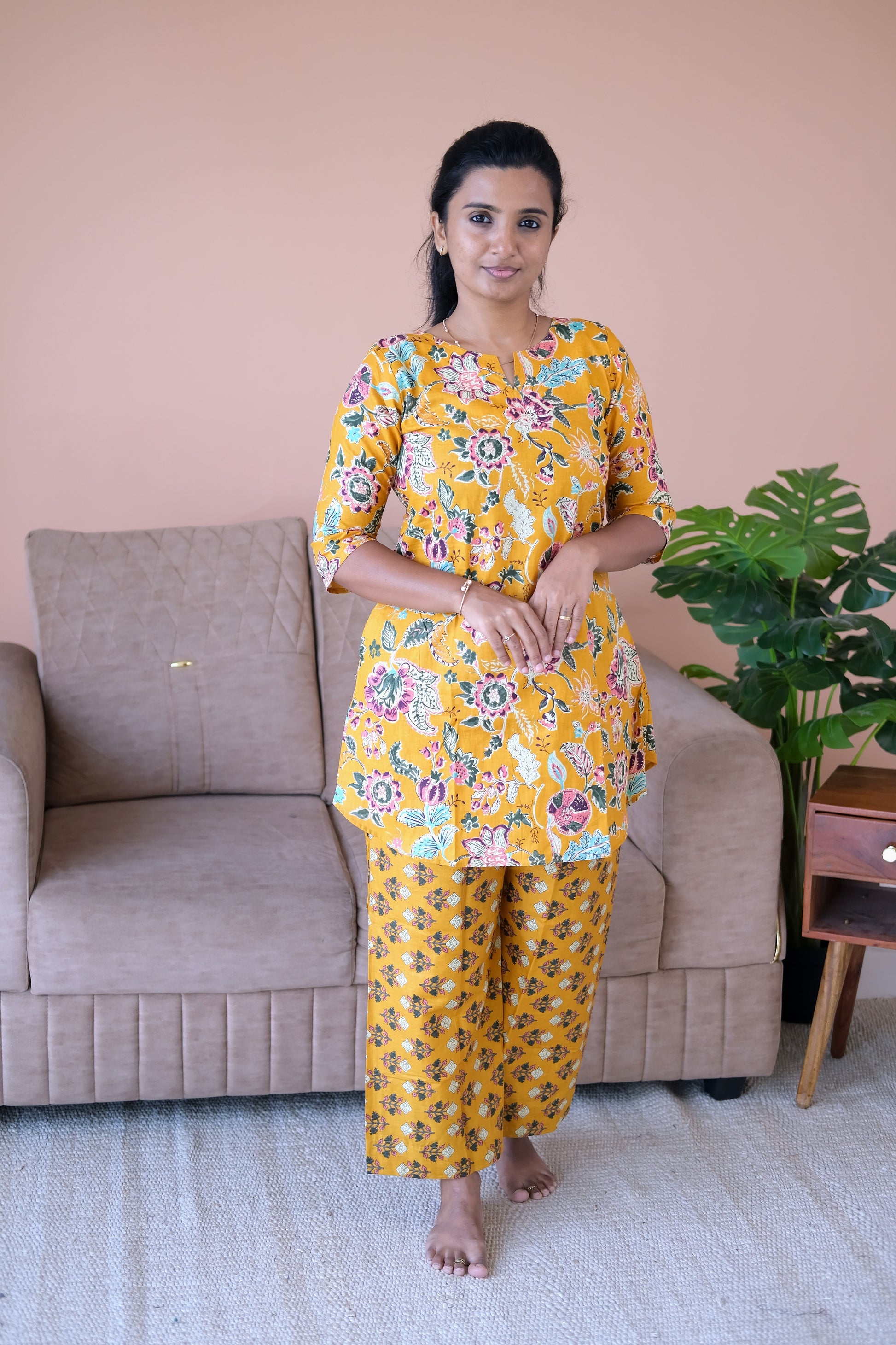 A woman wearing a golden mustard cotton night suit for women with floral prints and relaxed pants.