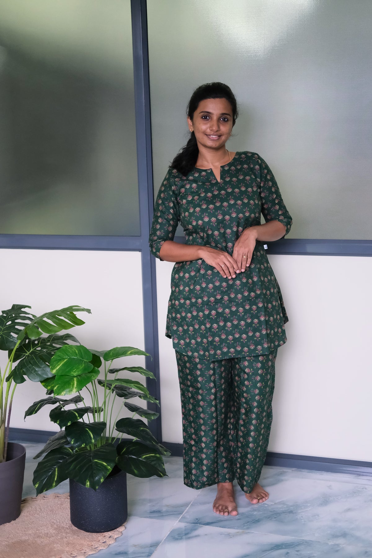 Woman wearing a deep green cotton night suit for women with a pink floral print and relaxed-fit pants.