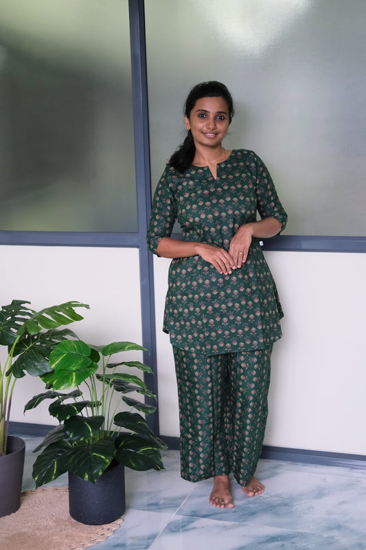 Woman wearing a deep green cotton night suit for women with a pink floral print and relaxed-fit pants.
