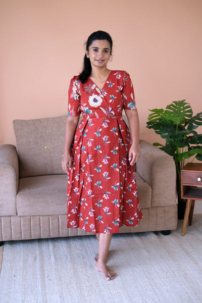 A woman wearing the Varsha rust red cotton midi nighty with a floral print and pleated waist.