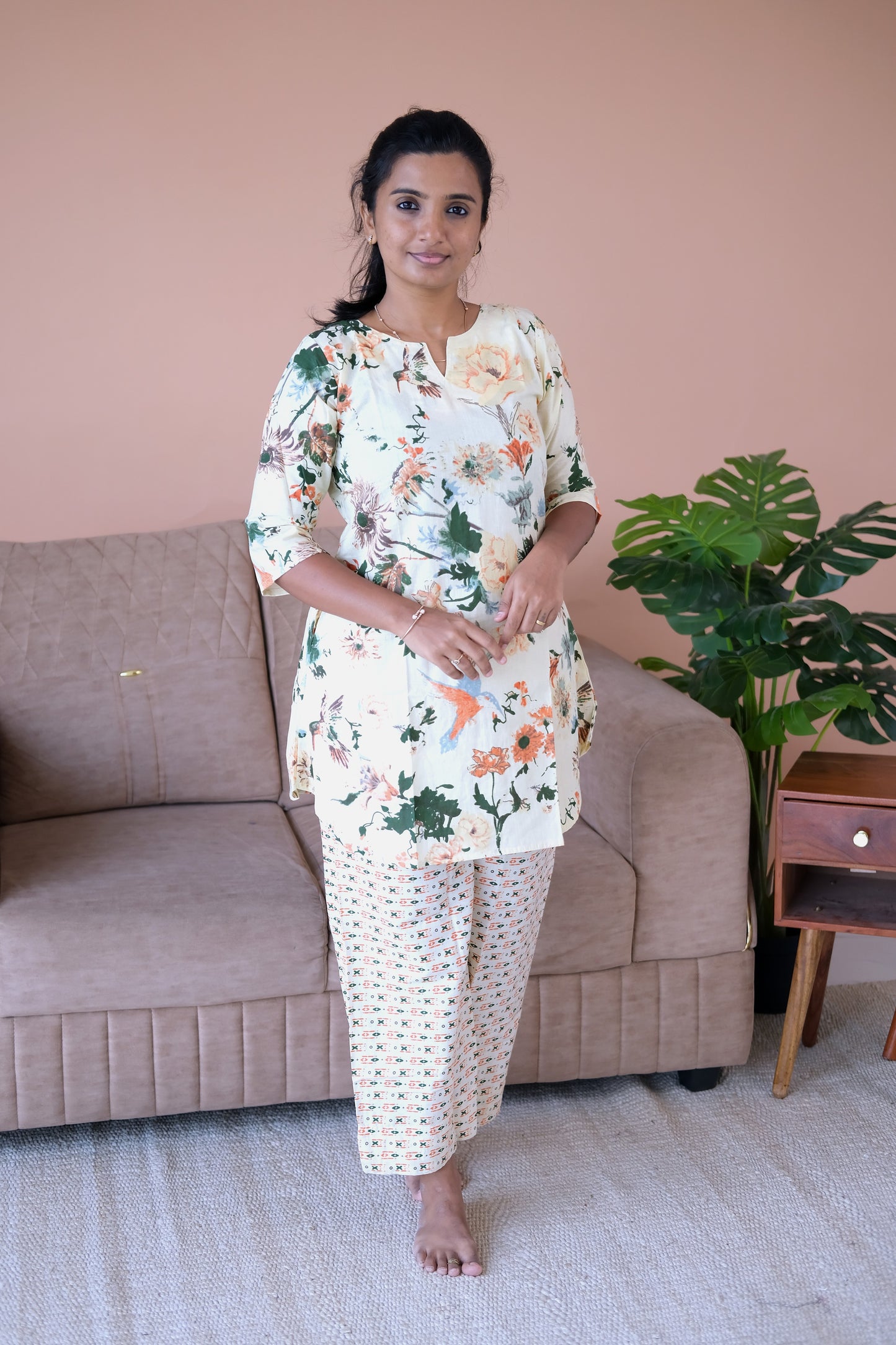 An ivory cotton night suit for women featuring a colorful floral and bird print tunic top paired with geometric patterned straight-leg pants.