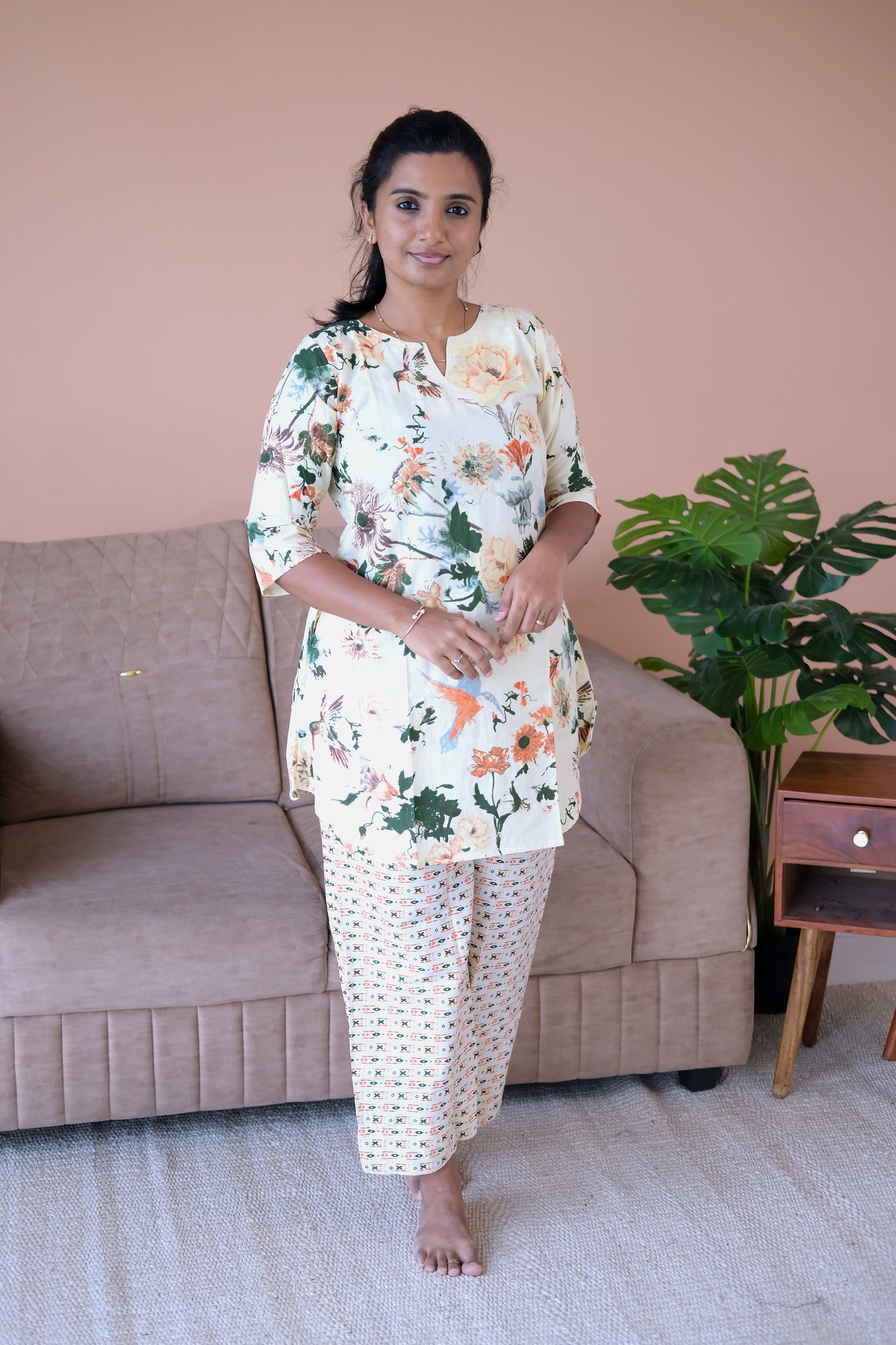 An ivory cotton night suit for women featuring a colorful floral and bird print tunic top paired with geometric patterned straight-leg pants.