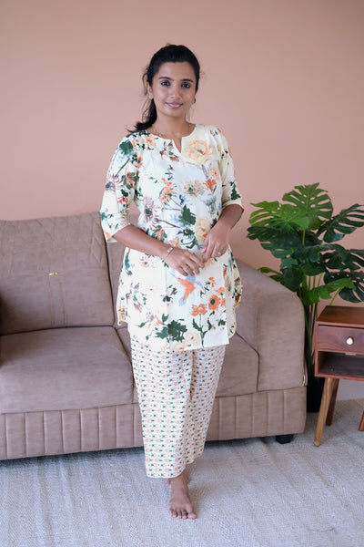 An ivory cotton night suit for women featuring a colorful floral and bird print tunic top paired with geometric patterned straight-leg pants.